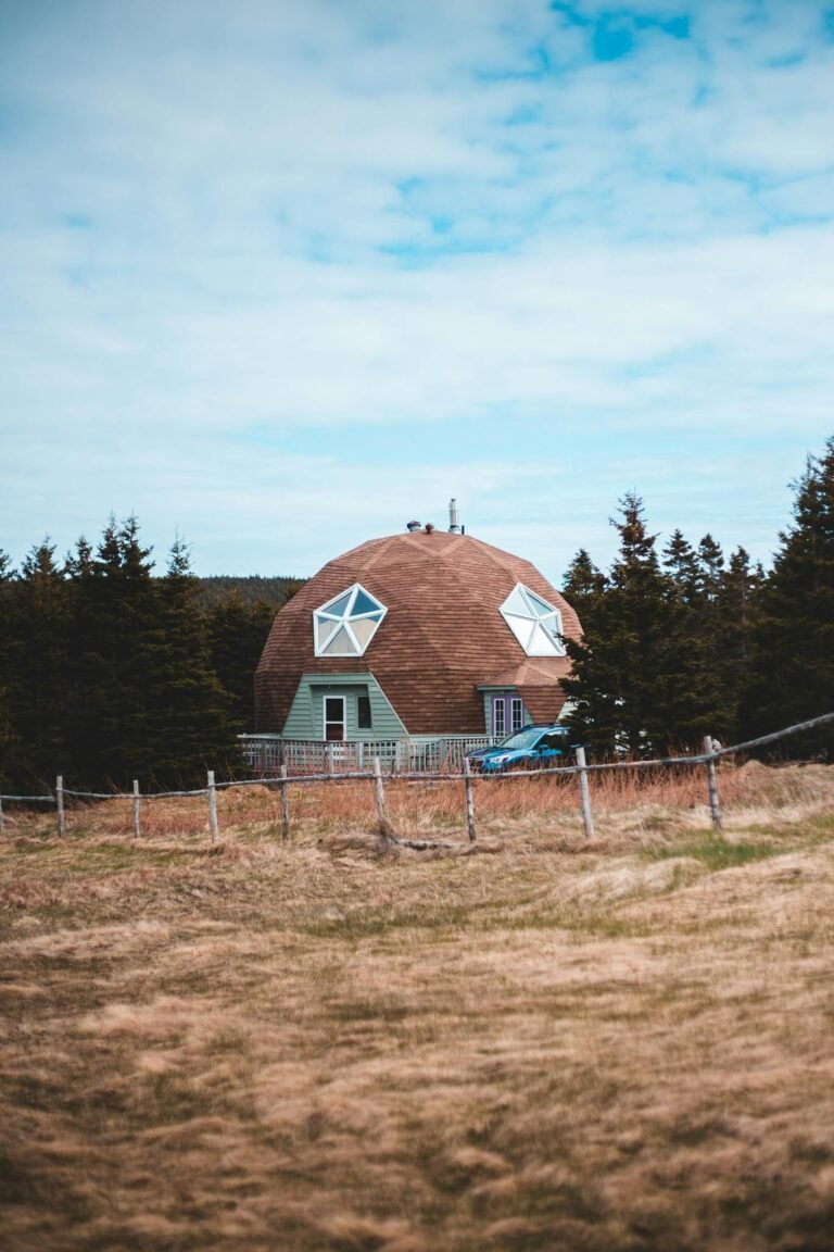 Exterior of creative contemporary residential house with poly angular piled roof of brown color and star shaped window located on grassy valley amidst firs and rural fence